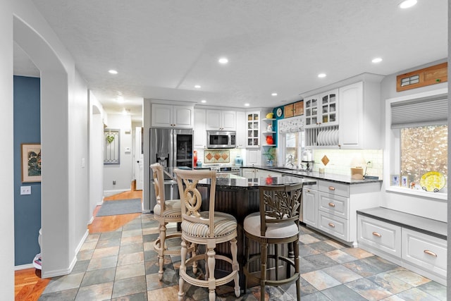 kitchen with white cabinetry, stainless steel appliances, a kitchen breakfast bar, decorative backsplash, and a kitchen island