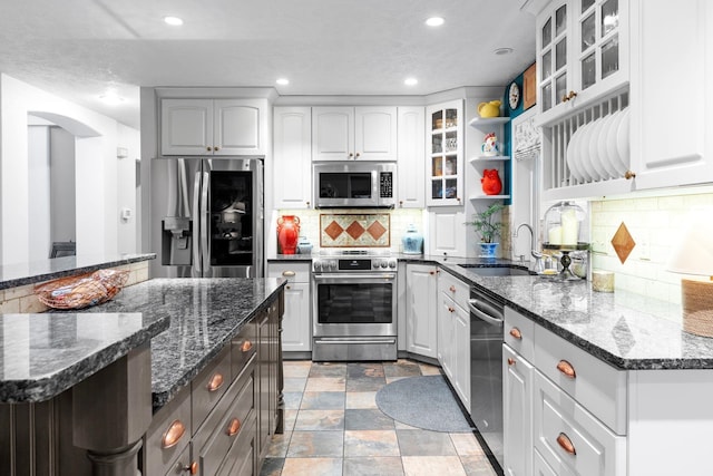 kitchen featuring appliances with stainless steel finishes, sink, dark stone countertops, white cabinets, and a kitchen island