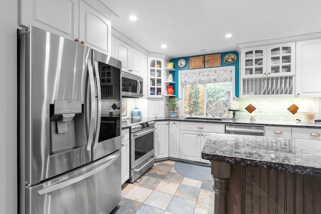 kitchen featuring decorative backsplash, dark stone counters, stainless steel appliances, sink, and white cabinets