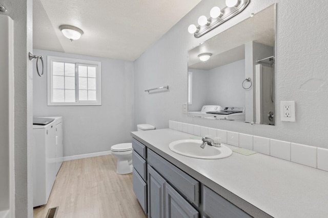 bathroom featuring hardwood / wood-style floors, vanity, toilet, independent washer and dryer, and a textured ceiling