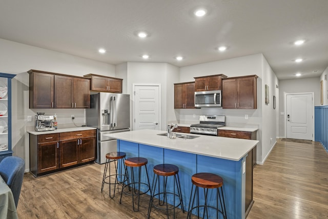 kitchen featuring a kitchen island with sink, sink, light wood-type flooring, and appliances with stainless steel finishes