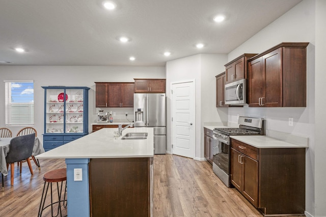 kitchen with appliances with stainless steel finishes, a breakfast bar, sink, light hardwood / wood-style flooring, and an island with sink