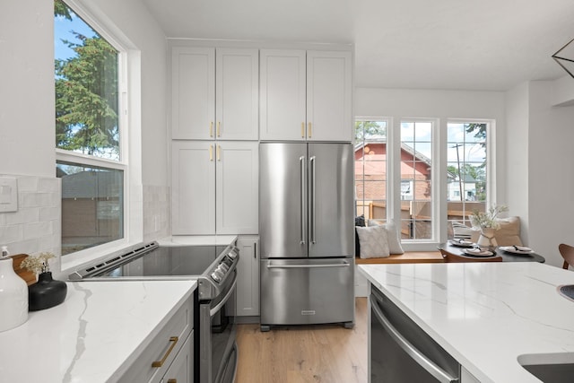 kitchen featuring light stone countertops, appliances with stainless steel finishes, tasteful backsplash, light hardwood / wood-style flooring, and white cabinetry