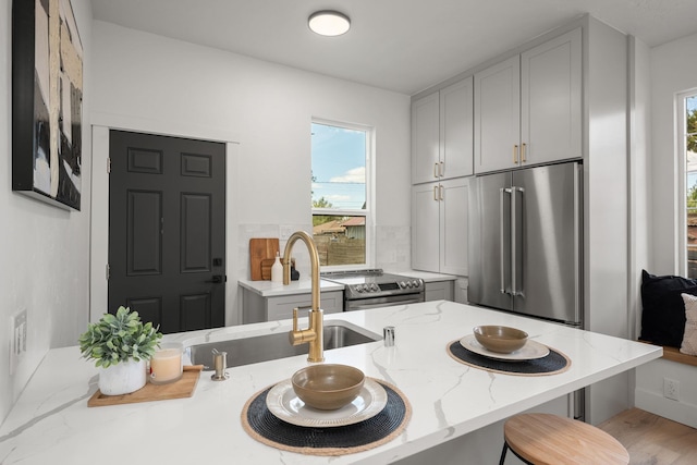 kitchen with light stone countertops, sink, a kitchen bar, appliances with stainless steel finishes, and light wood-type flooring