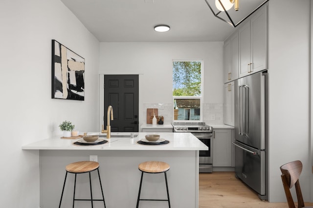 kitchen featuring sink, light hardwood / wood-style flooring, appliances with stainless steel finishes, a kitchen bar, and kitchen peninsula