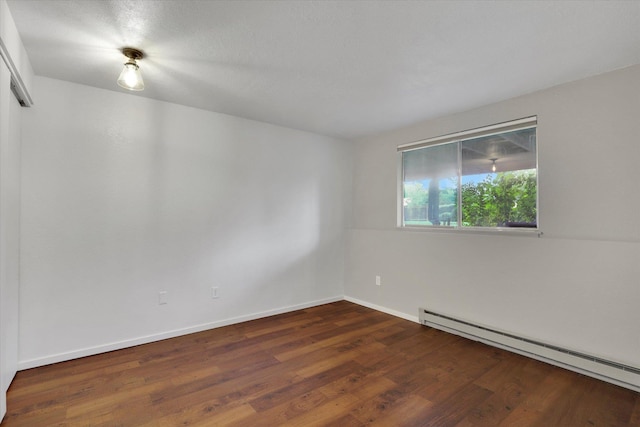 empty room with dark wood-type flooring and a baseboard heating unit