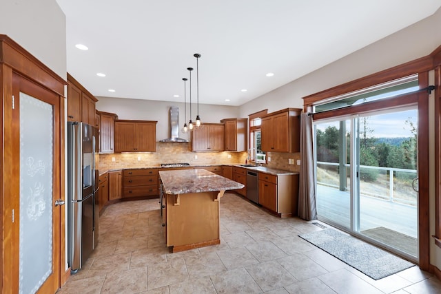 kitchen with light stone countertops, wall chimney exhaust hood, stainless steel appliances, a kitchen island, and hanging light fixtures