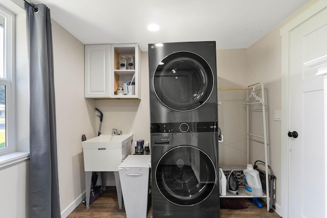 laundry room featuring dark wood-type flooring, stacked washing maching and dryer, and sink