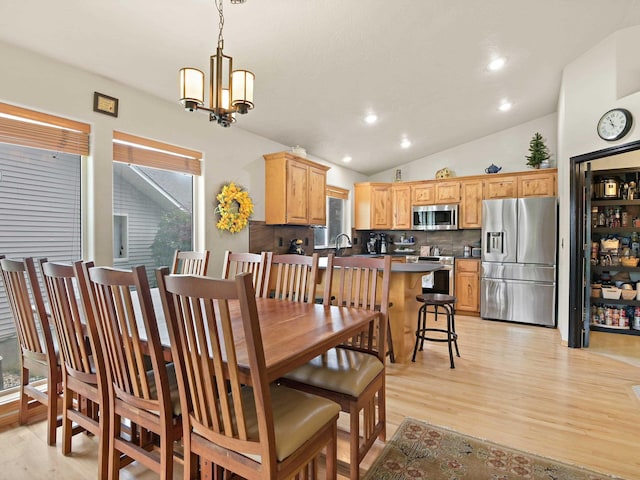 dining room featuring sink, light wood-type flooring, vaulted ceiling, and a notable chandelier