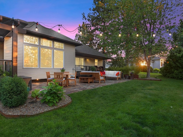 back house at dusk with outdoor lounge area, a patio area, and a lawn