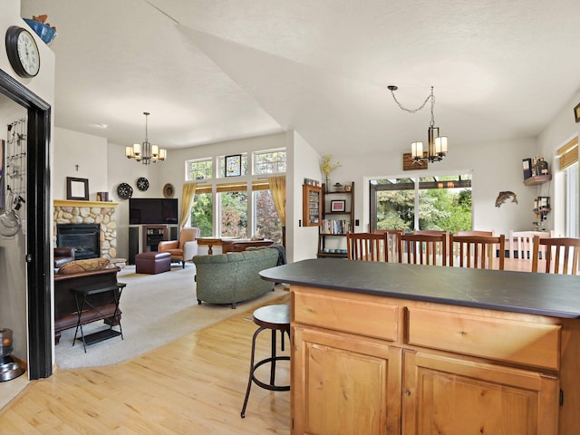 kitchen with lofted ceiling, a stone fireplace, light hardwood / wood-style flooring, decorative light fixtures, and a chandelier