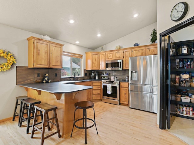 kitchen with decorative backsplash, kitchen peninsula, light wood-type flooring, stainless steel appliances, and sink