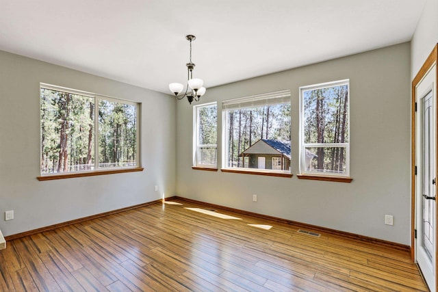 spare room with a healthy amount of sunlight, light wood-type flooring, and an inviting chandelier