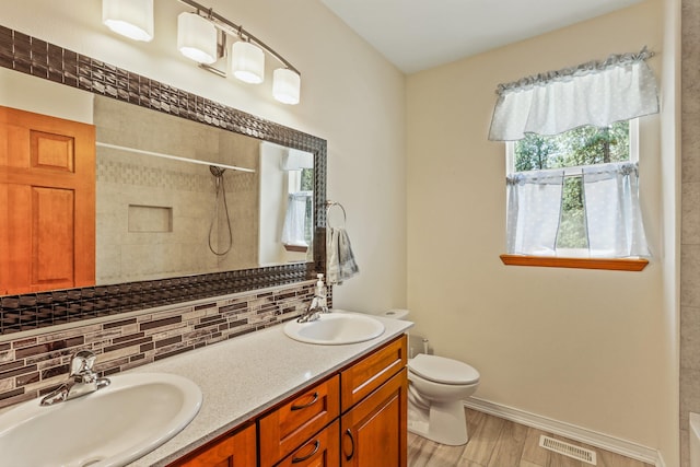 bathroom featuring vanity, toilet, tiled shower, and tasteful backsplash