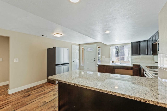 kitchen with light hardwood / wood-style flooring, light stone countertops, tasteful backsplash, kitchen peninsula, and stainless steel refrigerator