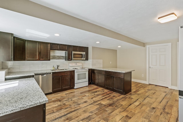 kitchen with kitchen peninsula, appliances with stainless steel finishes, decorative backsplash, light stone counters, and light hardwood / wood-style flooring