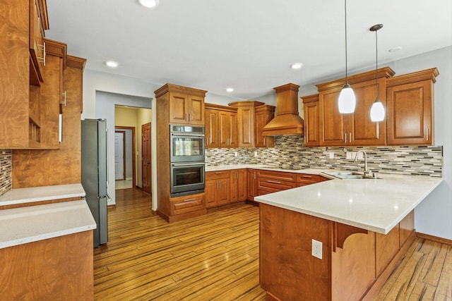 kitchen with kitchen peninsula, tasteful backsplash, custom range hood, sink, and decorative light fixtures