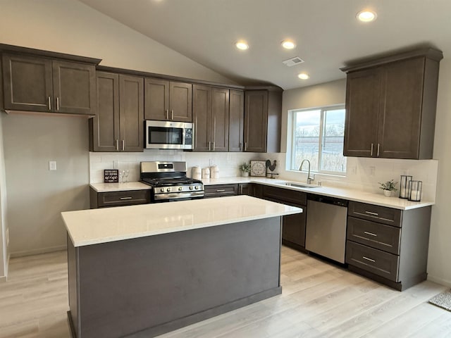 kitchen with sink, stainless steel appliances, a center island, light hardwood / wood-style floors, and vaulted ceiling