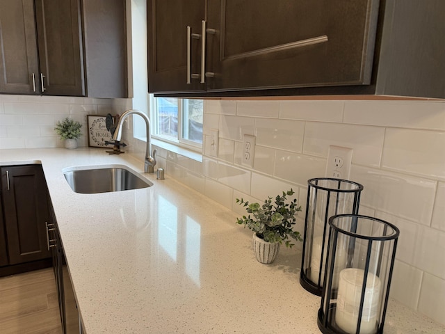 kitchen with a sink, light stone counters, stainless steel dishwasher, dark brown cabinetry, and decorative backsplash