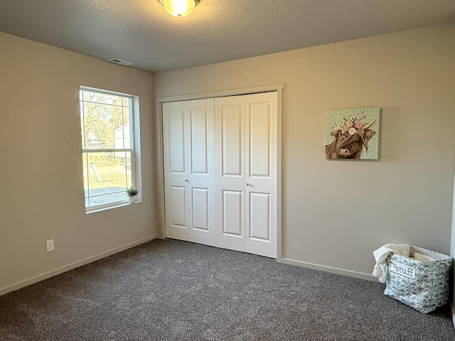 unfurnished bedroom featuring visible vents, a textured ceiling, dark carpet, a closet, and baseboards