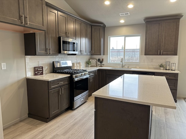 kitchen featuring visible vents, dark brown cabinets, light wood-style floors, stainless steel appliances, and a sink