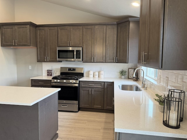 kitchen featuring light wood finished floors, lofted ceiling, a sink, stainless steel appliances, and dark brown cabinetry