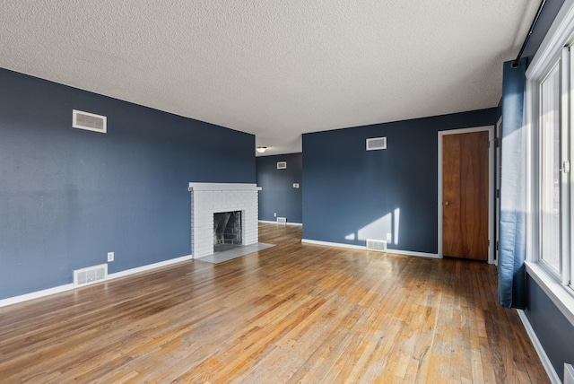 unfurnished living room featuring a textured ceiling, light hardwood / wood-style floors, and a brick fireplace