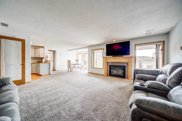 carpeted living room featuring a tile fireplace, plenty of natural light, and a textured ceiling