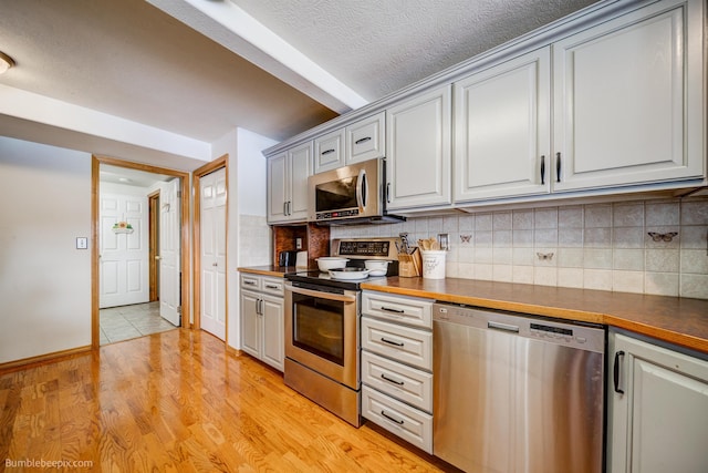 kitchen with butcher block countertops, a textured ceiling, decorative backsplash, appliances with stainless steel finishes, and light wood-type flooring