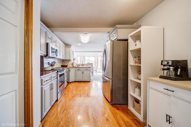 kitchen featuring appliances with stainless steel finishes, light wood-type flooring, backsplash, gray cabinetry, and a textured ceiling