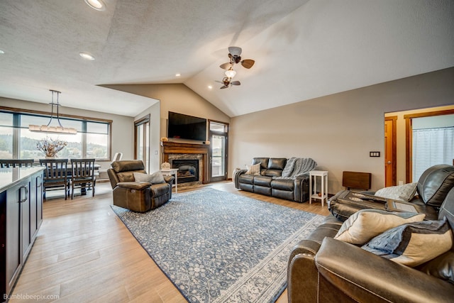 living room featuring a textured ceiling, ceiling fan, light hardwood / wood-style floors, and vaulted ceiling