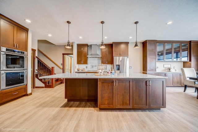 kitchen with appliances with stainless steel finishes, a center island with sink, hanging light fixtures, and wall chimney exhaust hood