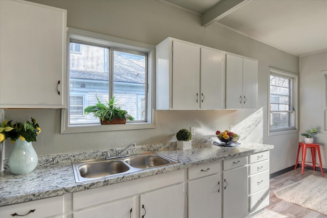 kitchen with light stone countertops, sink, beamed ceiling, white cabinets, and light hardwood / wood-style floors