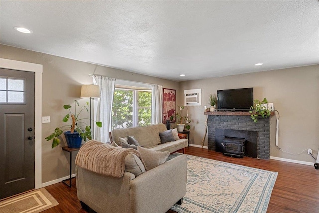 living room with a textured ceiling, a wood stove, a wall mounted AC, and dark wood-type flooring