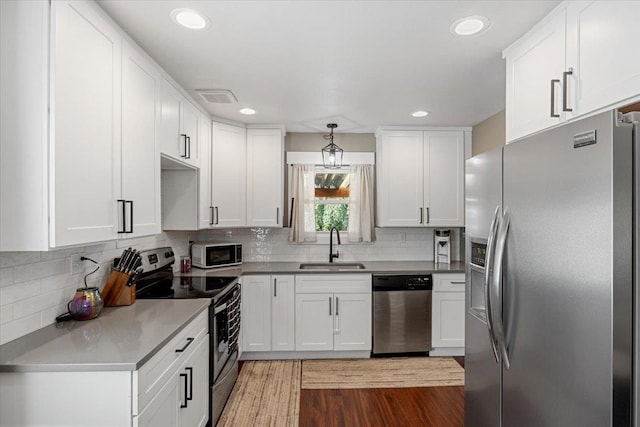 kitchen with backsplash, white cabinets, sink, hanging light fixtures, and stainless steel appliances