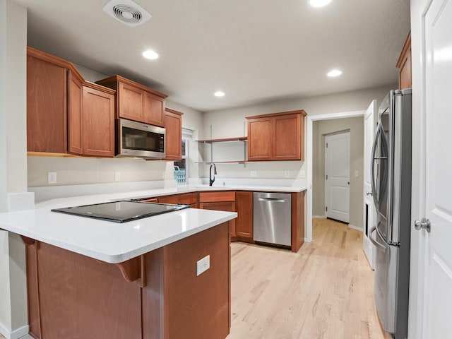 kitchen with kitchen peninsula, a kitchen breakfast bar, light wood-type flooring, stainless steel appliances, and sink