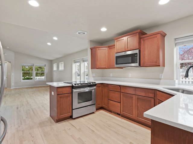 kitchen featuring lofted ceiling, sink, appliances with stainless steel finishes, light hardwood / wood-style floors, and kitchen peninsula