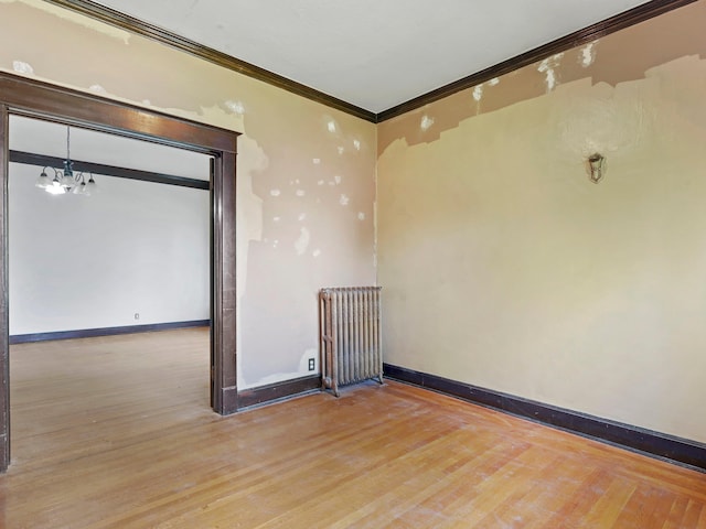 unfurnished room with hardwood / wood-style flooring, an inviting chandelier, radiator, and ornamental molding