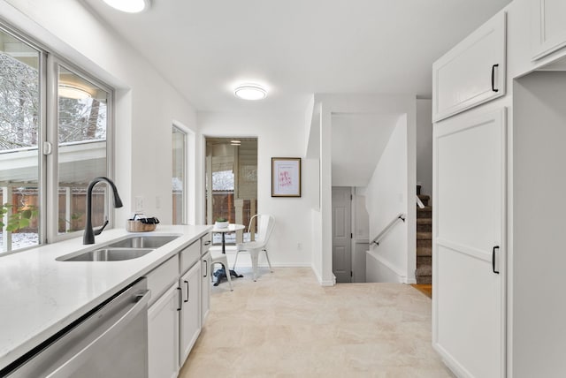 kitchen with light stone countertops, dishwasher, white cabinets, and sink