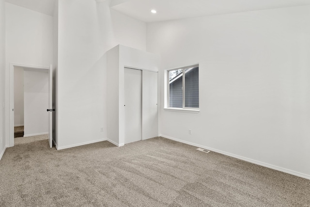 unfurnished bedroom featuring light carpet, a high ceiling, and a closet