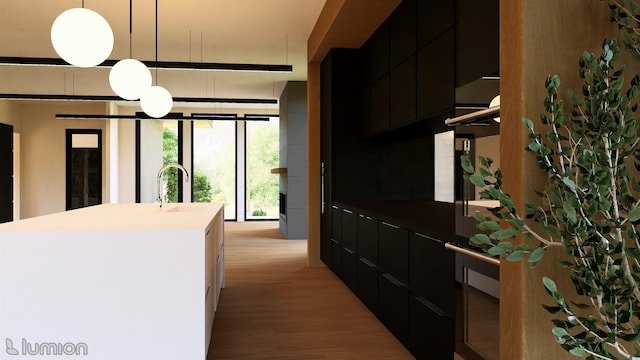 kitchen with light wood-type flooring, a center island with sink, hanging light fixtures, and sink