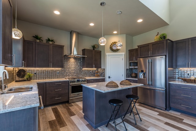 kitchen featuring a kitchen island, a sink, high quality appliances, dark brown cabinets, and wall chimney range hood