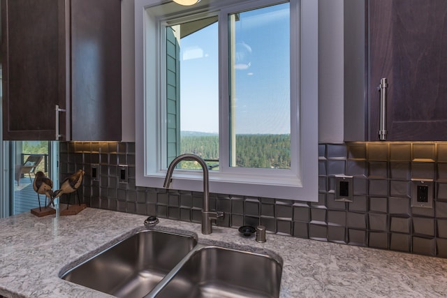 kitchen with light stone counters, backsplash, a sink, and dark brown cabinetry