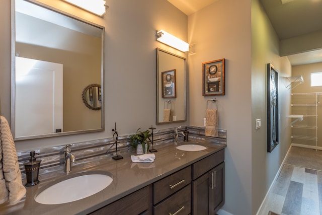 full bathroom featuring wood finished floors, a sink, baseboards, and double vanity