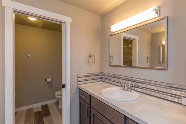 bathroom with baseboards, vanity, toilet, and wood finished floors