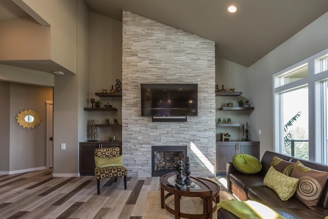 living room with high vaulted ceiling, a tiled fireplace, wood finished floors, and baseboards