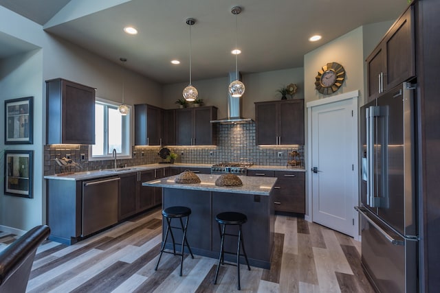 kitchen with a sink, appliances with stainless steel finishes, wall chimney range hood, and dark brown cabinetry