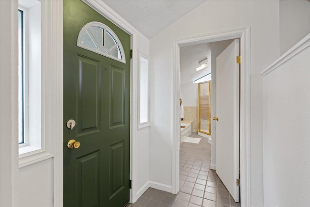 foyer featuring light tile patterned flooring, lofted ceiling, and a textured ceiling