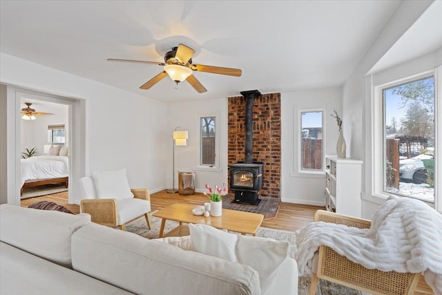 living room with a wood stove, ceiling fan, and light wood-type flooring