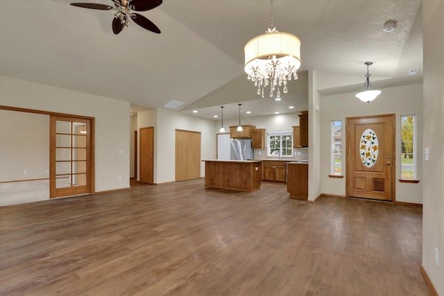 unfurnished living room featuring wood-type flooring, ceiling fan with notable chandelier, and vaulted ceiling